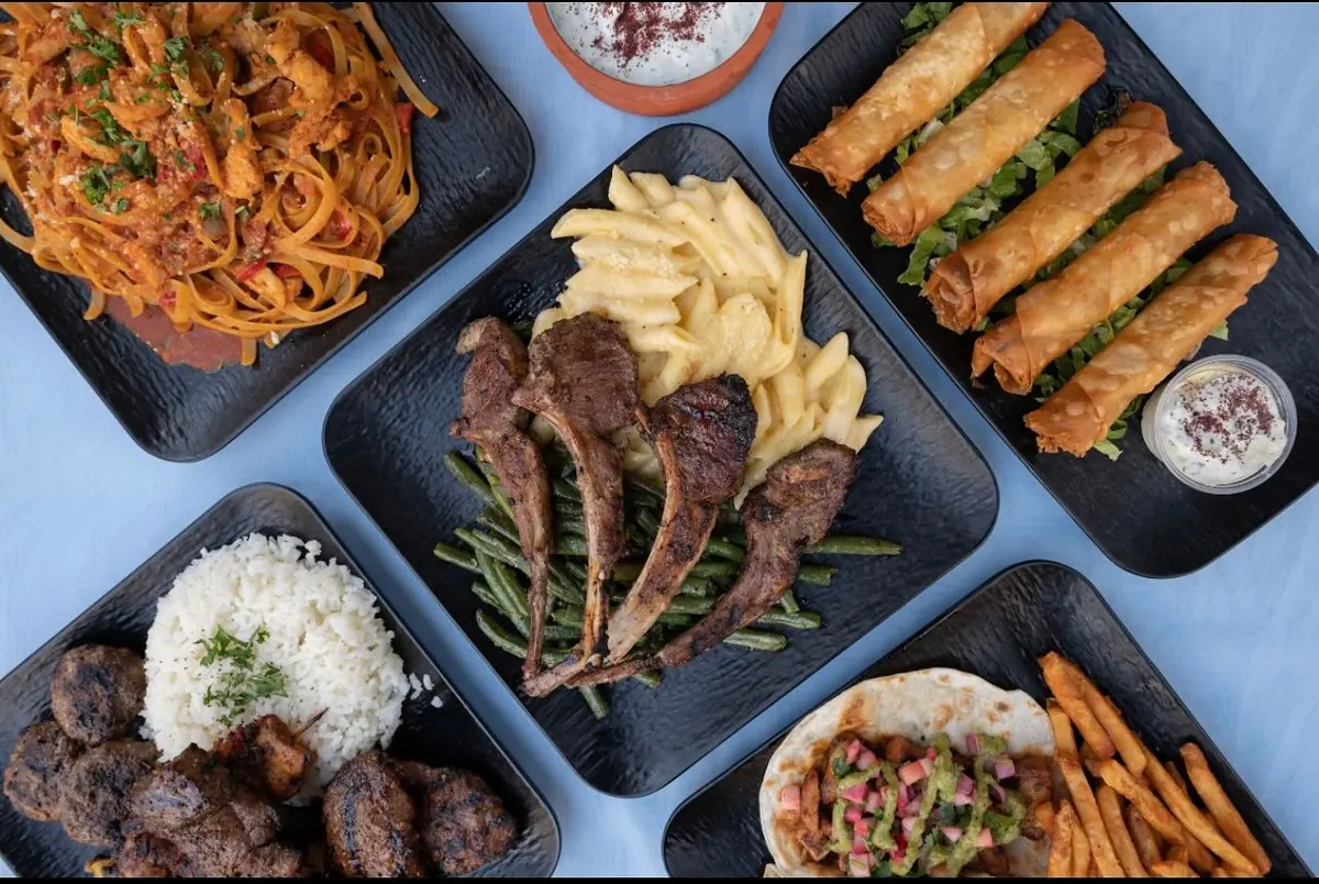An overhead spread of lamb chops, pasta, golden rolls, and a gyro with fries